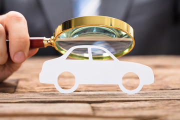 Businessman's Hand Examining Paper Car With Magnifying Glass