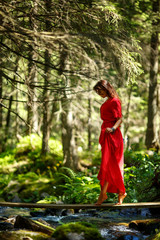 Portrait of romantic woman in fairy forest. Young woman in red dress standing in the woods