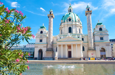 Facade of Karlskirche (St. Charles's Church) against blue sky, white clouds and a pond with water...