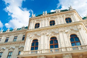 Fototapeta na wymiar View from below on the intricate details of the magnificent white and clean Upper Belvedere palace with its windows, balcony, beautiful moulding against blue vibrant sky with clouds on a summer day