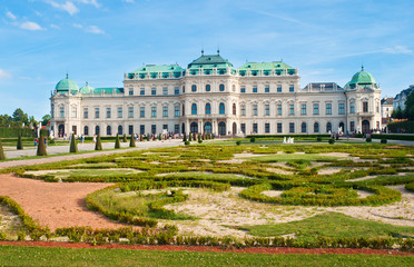 Naklejka premium Close view on magnificent Belvedere palace surrounded by a beautiful trimmed flowerbed and lawn against a blue vibrant sky with several solitary clouds. Summer, Vienna