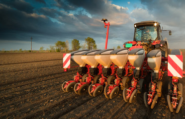 Farmer with tractor seeding - sowing crops at agricultural field in spring