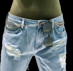 Stylish light blue jeans with chain accessories and sunglasses on waist against black background. Vintage denim with skinny and low-rise pattern