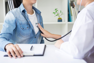 Doctor listening to cheerful young patients chest with stethoscope in his office at the hospital