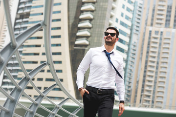 Young stylish handsome businessman is walking near the fence in the beautiful city.