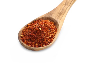 pile crushed red cayenne pepper, dried chili flakes, seeds and wooden spoon isolated on white background