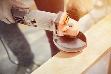 A man holds and grinds a piece of wood with a grinder with a lot of dust