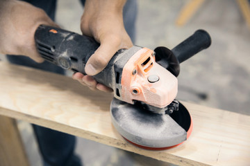 A man holds and grinds a piece of wood with a grinder with a lot of dust