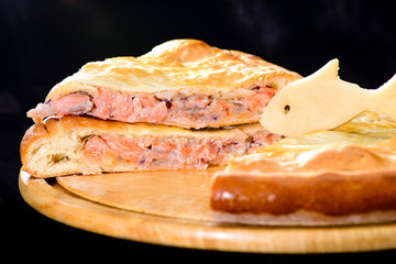close-up delicious hot sliced fish pie on wooden board, dark background