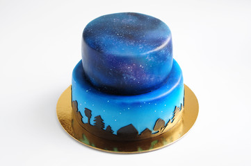 Artistic two-tiered cake with the image of the cosmos drawn by airbrush. Galaxy, stars in the night sky and silhouettes of trees. Cutout. Picture for a menu or a confectionery catalog.
