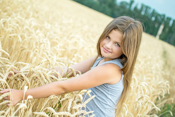 Portrait of slavic beautiful little girl with long hair touching wheat ears and looking in camera in the field on a summer day. The concept of growth, purity and youth