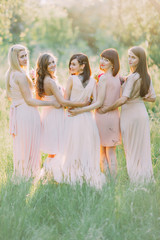 The back photo of the bride and her bridesmaids looking behind in the sunny forest. The black...