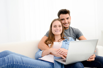 portrait of young and happy couple at home making project for future with laptop computer on internet