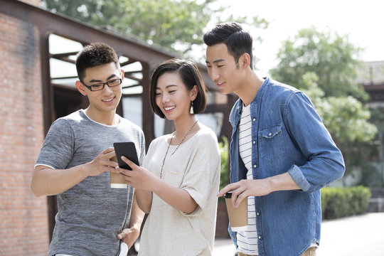 Smiling friends using a smartphone outdoors
