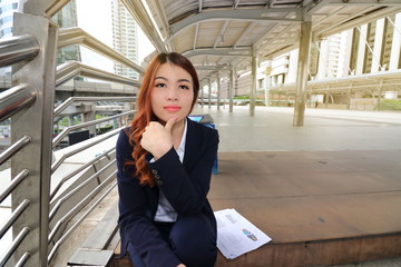 Portrait of attractive young Asian businesswoman sitting on stair way and looking on camera in urban building background.