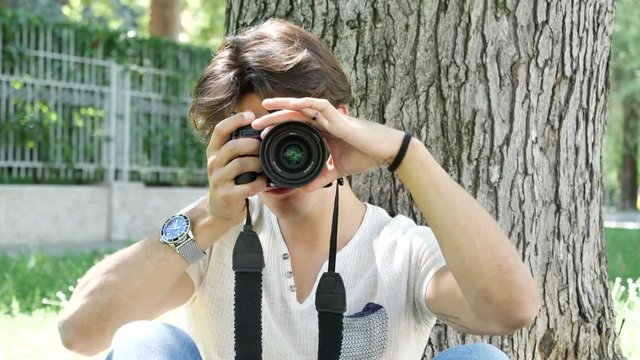 Handsome young male photographer taking photograph with professional photo camera hanging from his neck