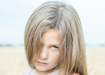 Portrait of adorable serene little girl with beautiful long hair on a summer day with blue sky and wheat field background
