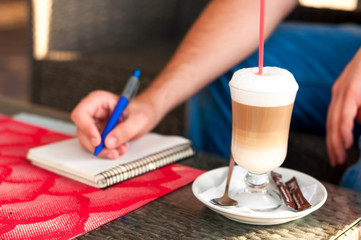 Man leafs through the diary and drinking coffee latte