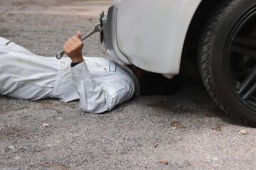 Side view of mechanic in white uniform lying down and fixing under car. Auto repair service.