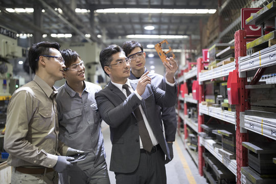 Businessman and engineers examining machine parts in the factory