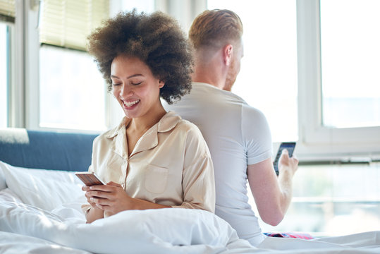 Couple Sitting In Bed, Texting On The Mobile Phone, Turned Backs To Each Other