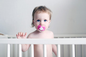 Little 1 years baby girl with dummy in white bed