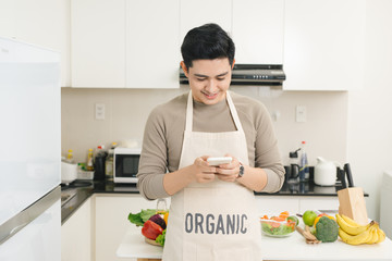 Handsome asian man texting with his smartphone in kitchen