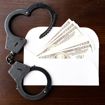 the envelope with dollars money and steel police handcuffs on wooden table, top view. Concept of bribery