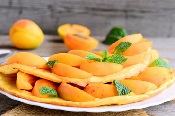 Homemade omelette or omelet stuffed with fresh apricot slices and mint on a white serving plate. How to make an omelette with filling. Summer delicious breakfast for the whole family. Closeup