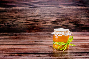 Glass jar with apricot jam with half apricot on wooden background.