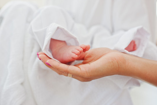 Close-up photo of small legs of a newborn baby on mother's hands.
