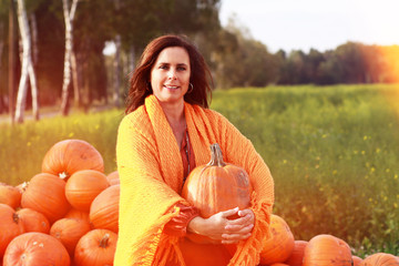 Attraktive Frau mittleren Alters vor vielen orangen Kürbissen im Herbst