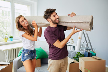 Portrait of a cute young couple carrying a rug together while moving in to new apartment
