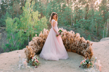Bride with rustic bridal bouquet stands on the rock. Wedding ceremony, decoration