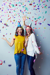 Two gorgeous young ladies celebrating party laughing and raising arms in birthday hats with...