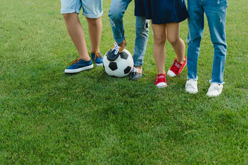 Obraz premium Cropped shot of children standing with soccer ball on green grass