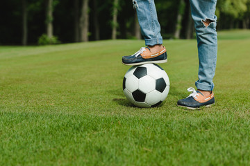 Close-up partial view of kid standing with soccer ball on green meadow