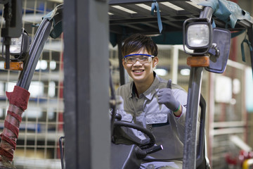 Young workman driving forklift in the factory