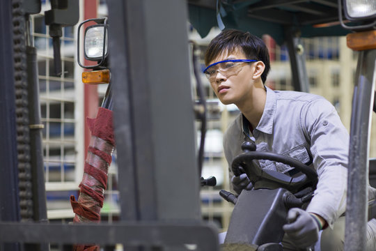 Young workman driving forklift in the factory