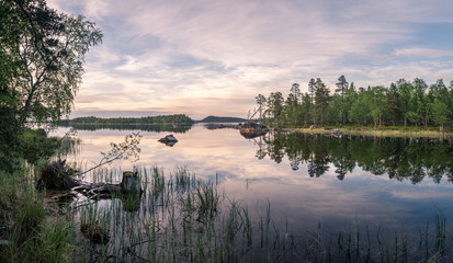 Panorama of calm lake at Lapland in midnight sun time. Rocks in front.