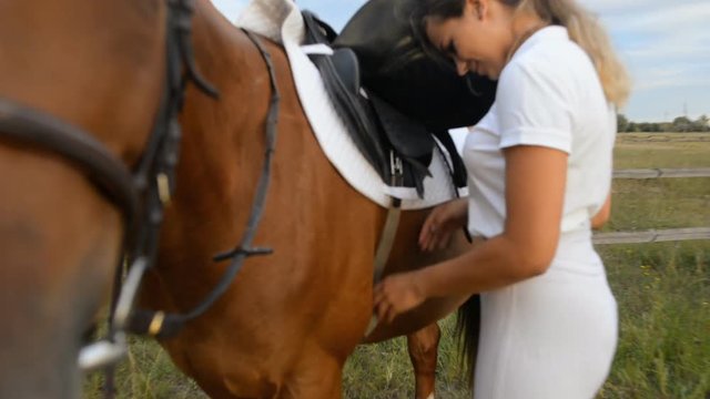 Young woman jockey dresses a saddle on her horse