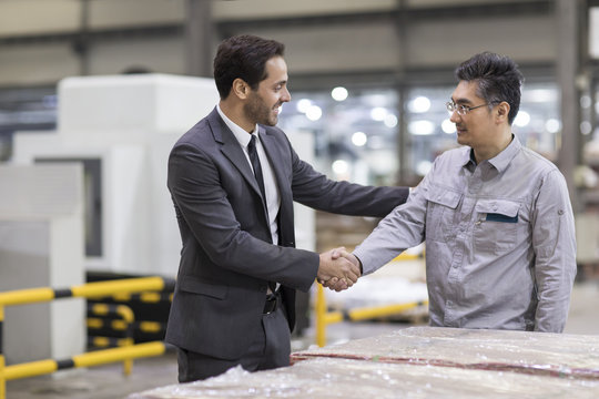 Businessman and engineer shaking hands in the factory
