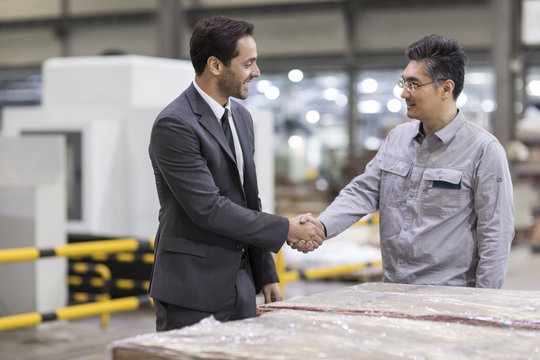 Businessman and engineer shaking hands in the factory