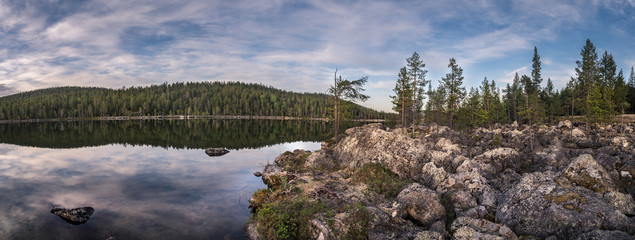 Panorama of calm lake at Lapland in midnight sun time. Rocks in front.