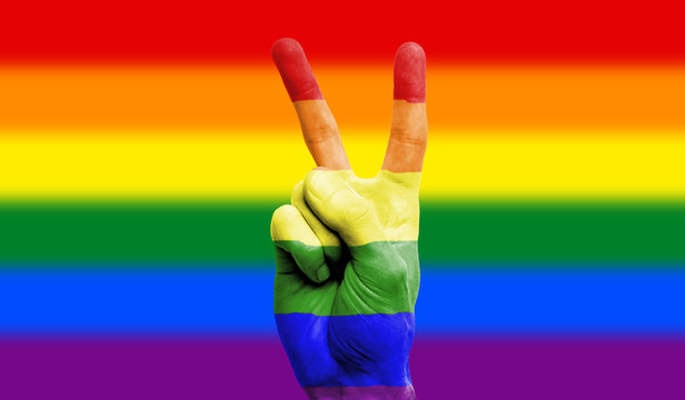 Pride flag painted on man's hand showing victory sign
