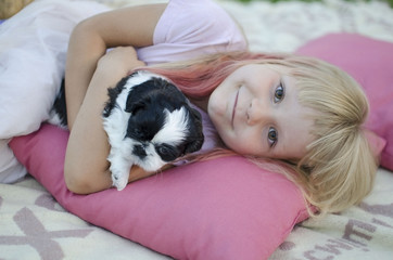 Little girl lies on the pink pillow. Cute blonde girl with black and white shi tzu puppies. Smiling blond girl 5 years old  