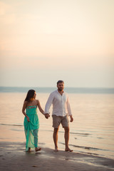 Enamored spouses hold each other's hands, a couple strolls along the beach in the evening, the sun goes over the horizon, the husband and wife take the day off together