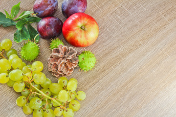Naklejka na ściany i meble Autumn fruits, cone, chestnuts, apple, plum and grapes on wood background with space for text