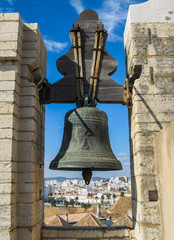 Obraz premium Old iron church bell and Faro's cityscape in the background at the top of Faro's Cathedral