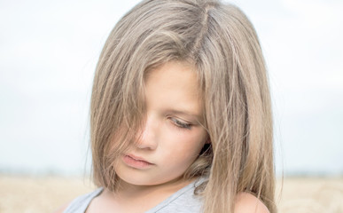 Portrait of adorable sad little girl with beautiful long hair on a summer day with blue sky and wheat field background